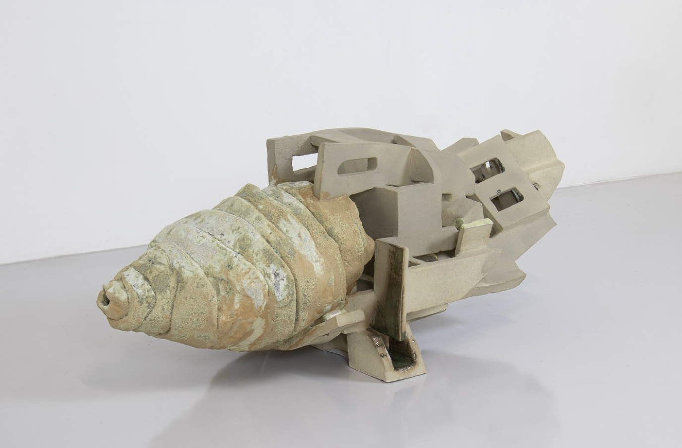 Beige-weiße Keramikskulptur mit spiralförmigem Muschelteil und eckiger Struktur auf weißem Boden